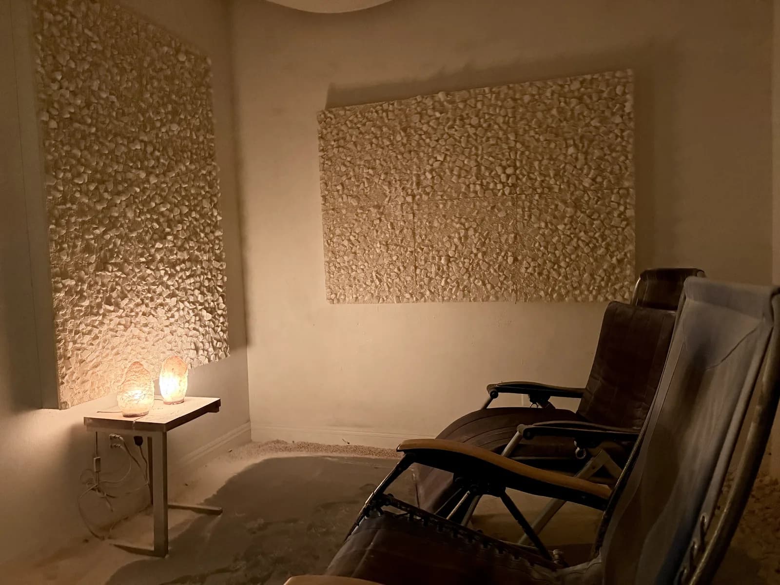 Adult Himalayan salt suite with amber walls, a backlit salt-brick feature, white lounge chairs, and salt across the floor. No people are shown.