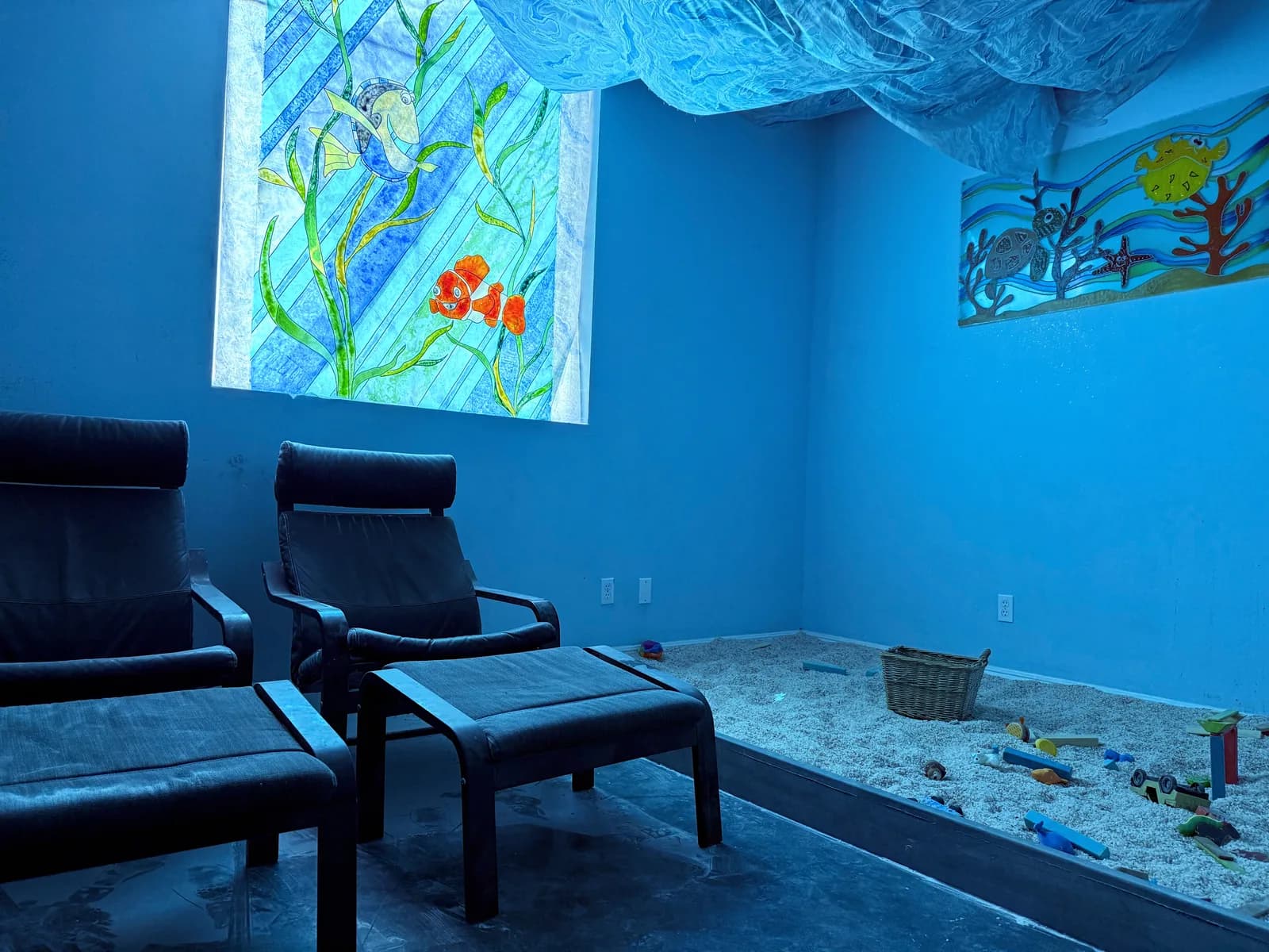 Children’s Himalayan salt suite with an underwater mural, pink salt on the floor, a small wooden bench, and a floor cushion. No people are shown.